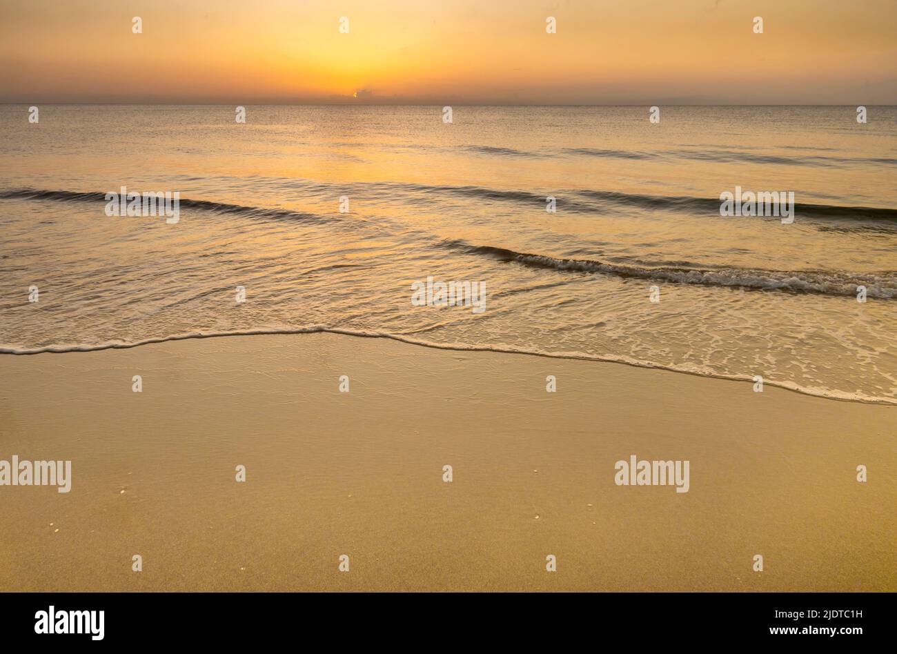 Surf paisible sur l'océan se lavant sur la plage au lever du soleil Banque D'Images