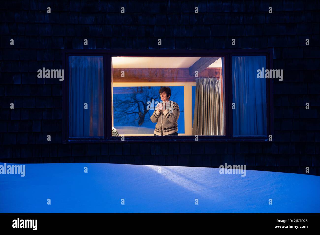 Femme regardant à travers la fenêtre au crépuscule en hiver Banque D'Images