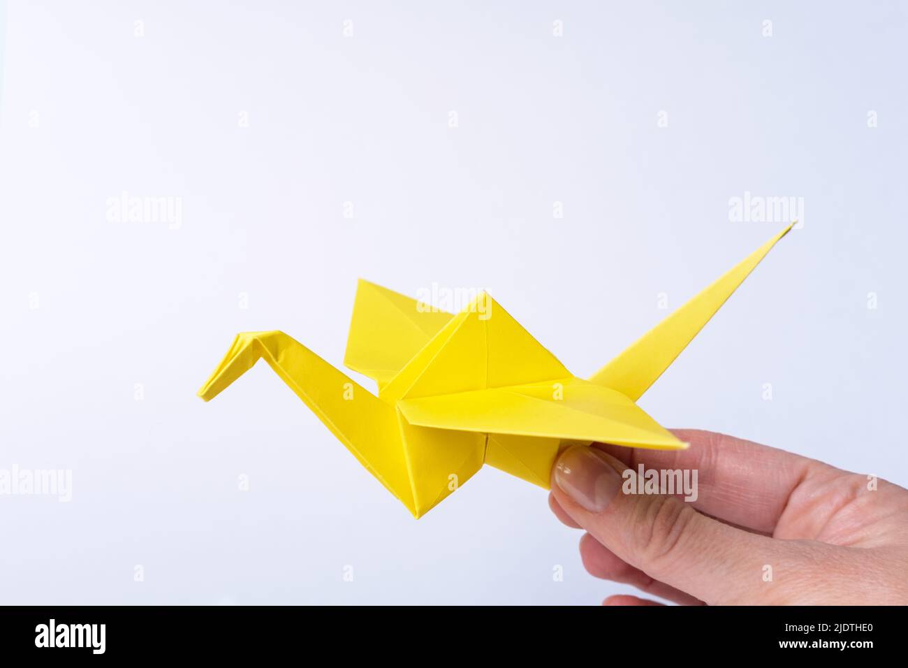 Main tenant un oiseau jaune en papier sur un fond clair. Grue en papier comme symbole de paix. Papier origami. Artisanat en papier avec des enfants. Banque D'Images