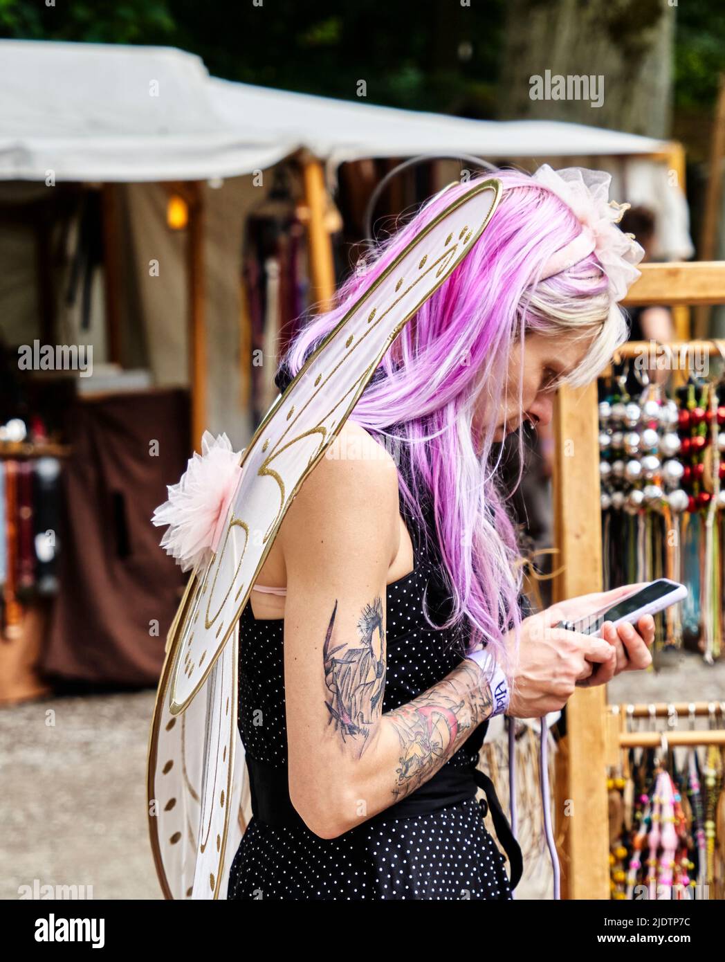 Pattensen, Allemagne, 4 juin 2022: Femme d'âge moyen avec des ailes de fées et des cheveux violets parlant sur son téléphone cellulaire au festival Fantasy en Allemagne Banque D'Images