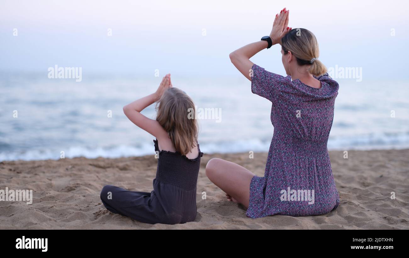 Maman et fille faisant du yoga et assis en position lotus sur la vue arrière de bord de mer Banque D'Images