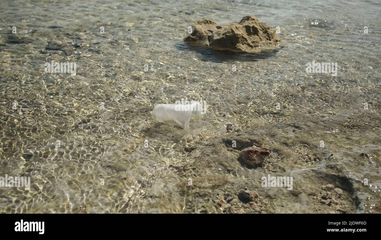 La tasse en plastique transparent est transportée par le vent jusqu'à la mer dans la zone côtière. Pollution plastique de la zone de surf. Mer rouge, Égypte Banque D'Images