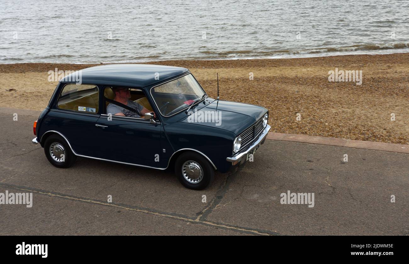 Classic Blue Leyland Mini étant conduit le long de front de mer promenade océan en arrière-plan. Banque D'Images