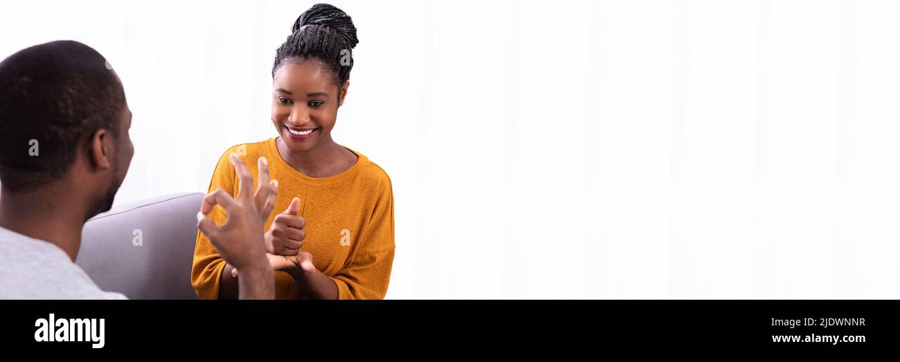 Smiling Young Couple Sitting on Sofa Communication avec les langues des signes Banque D'Images