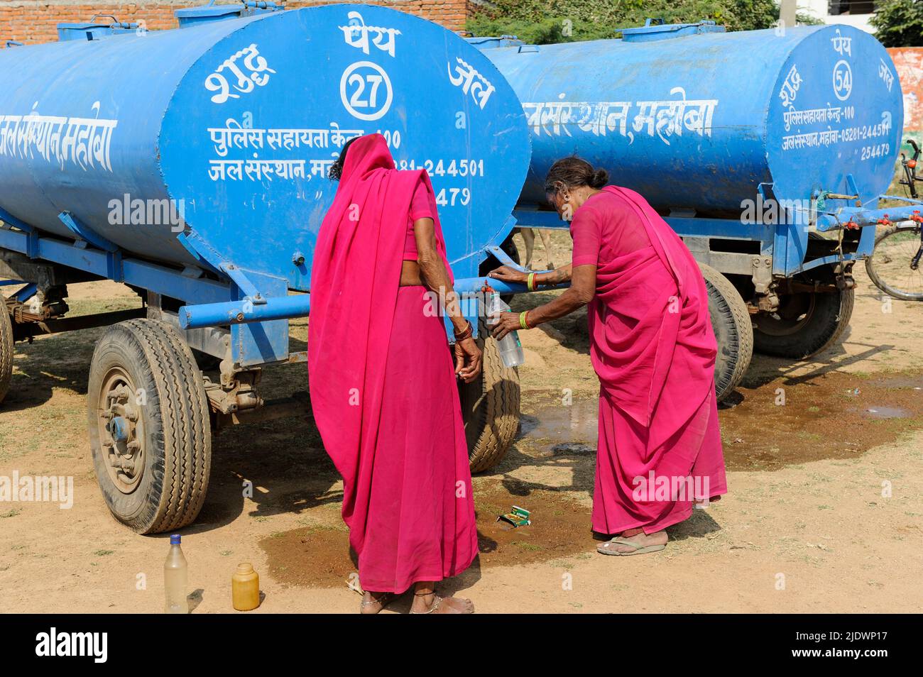 INDE, Uttar Pradesh, Bundelkhand, Mahoba, pénurie d'eau, Femmes en saree rose au réservoir d'eau bleu remplissant la bouteille en plastique avec de l'eau potable, lors d'un rassemblement de femmes mouvement Gulabi Gang Banque D'Images