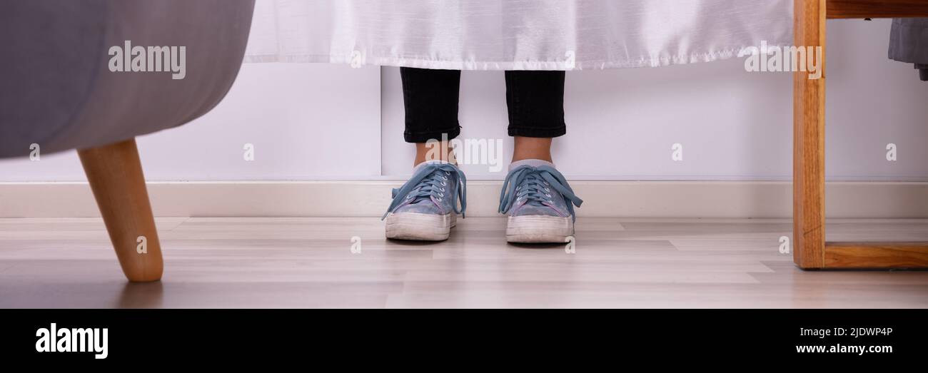 La section basse d'un Girl's pieds derrière le rideau sur plancher de bois franc Banque D'Images
