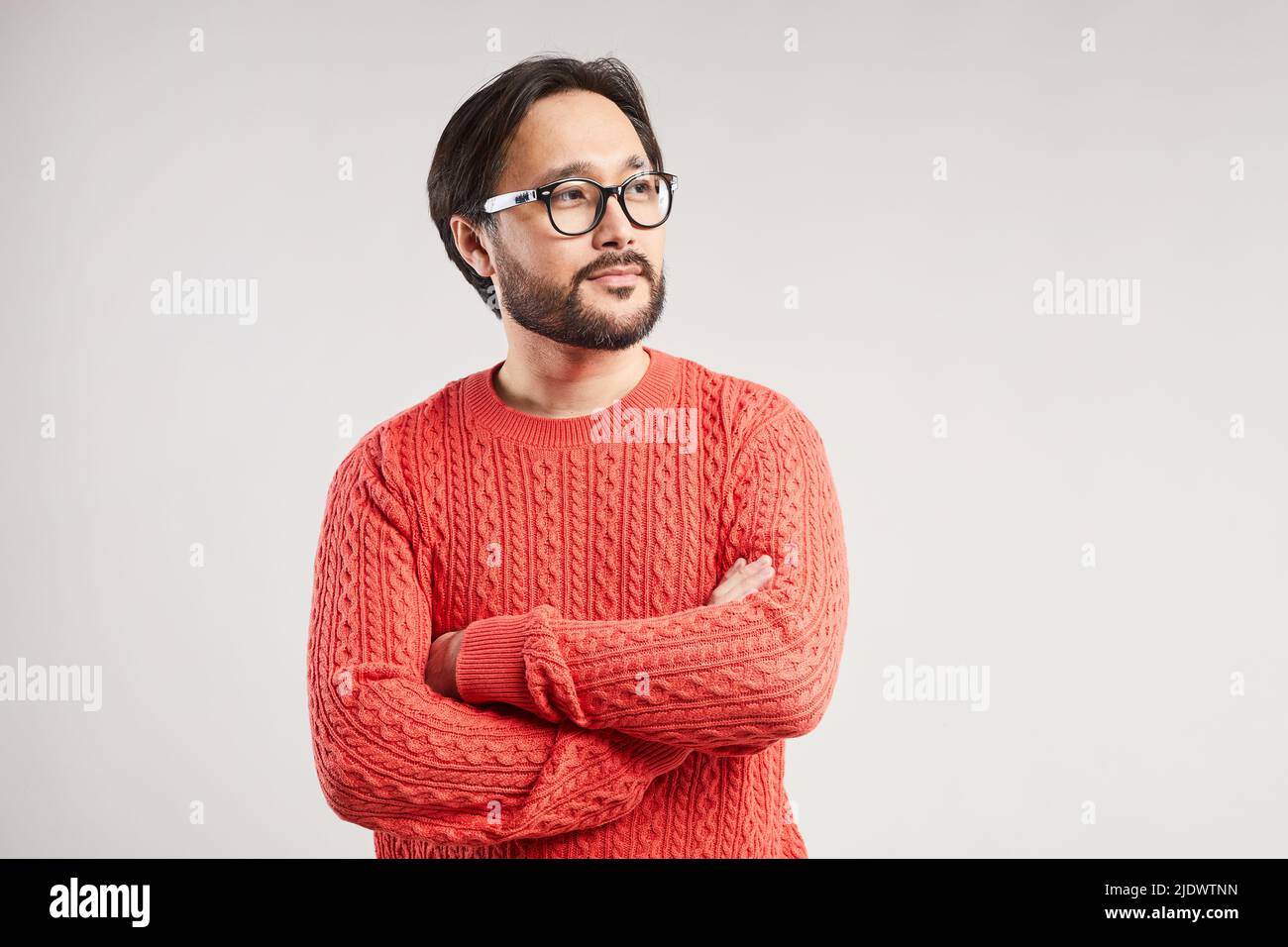 Content jeune homme asiatique rêveur avec une barbe et une moustache fraîches portant un pull chaud croisant les bras sur la poitrine Banque D'Images