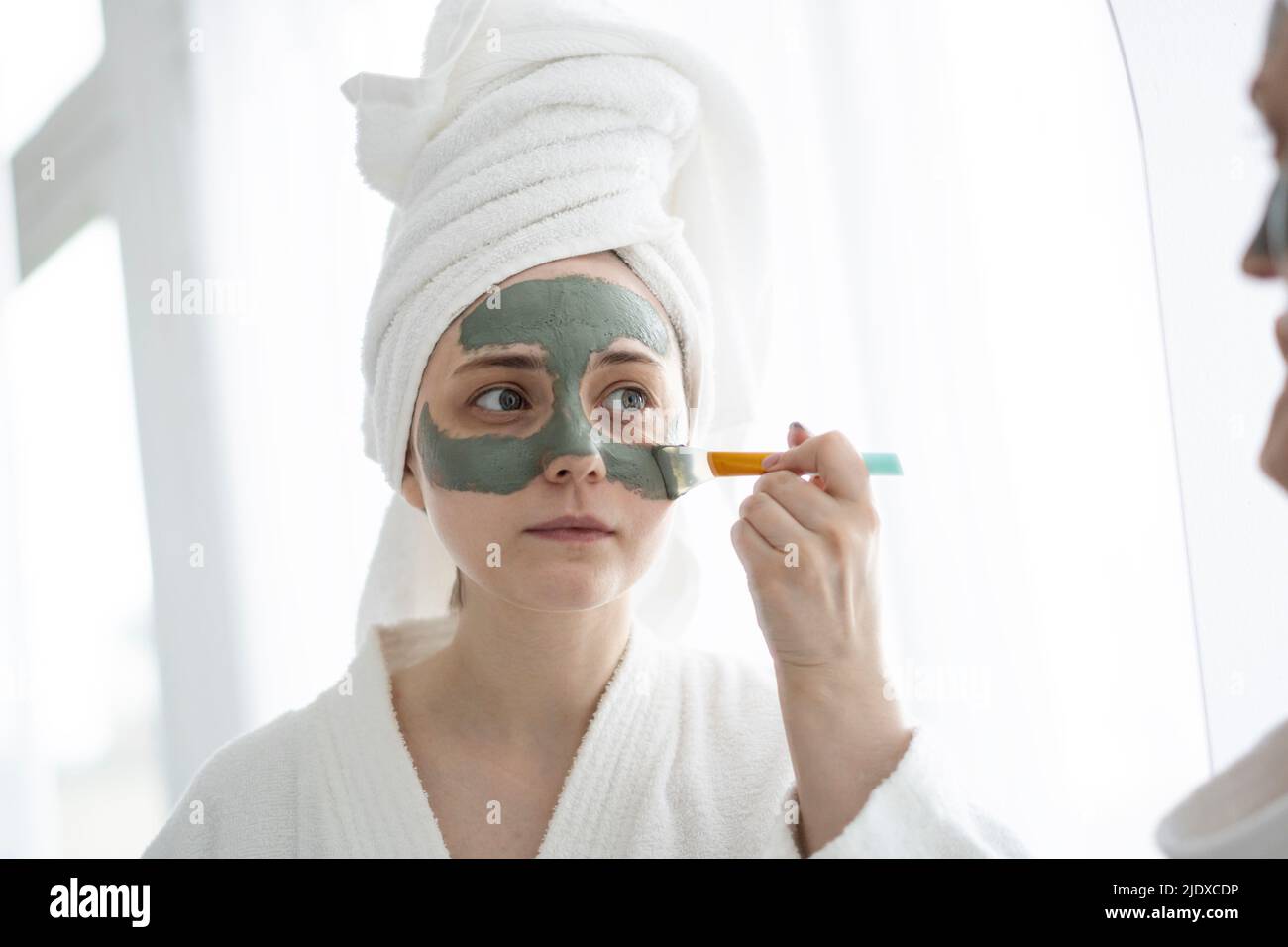 Jeune femme avec brosse appliquant un masque facial sur le visage à la maison Banque D'Images