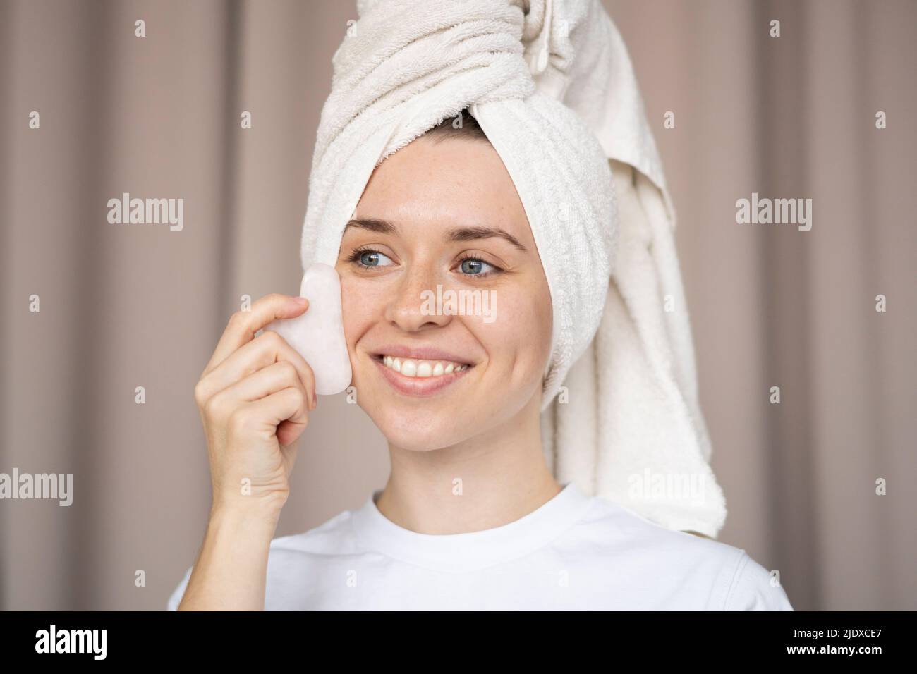 Une femme heureuse massante le visage avec la pierre de SHA gua à la maison Banque D'Images