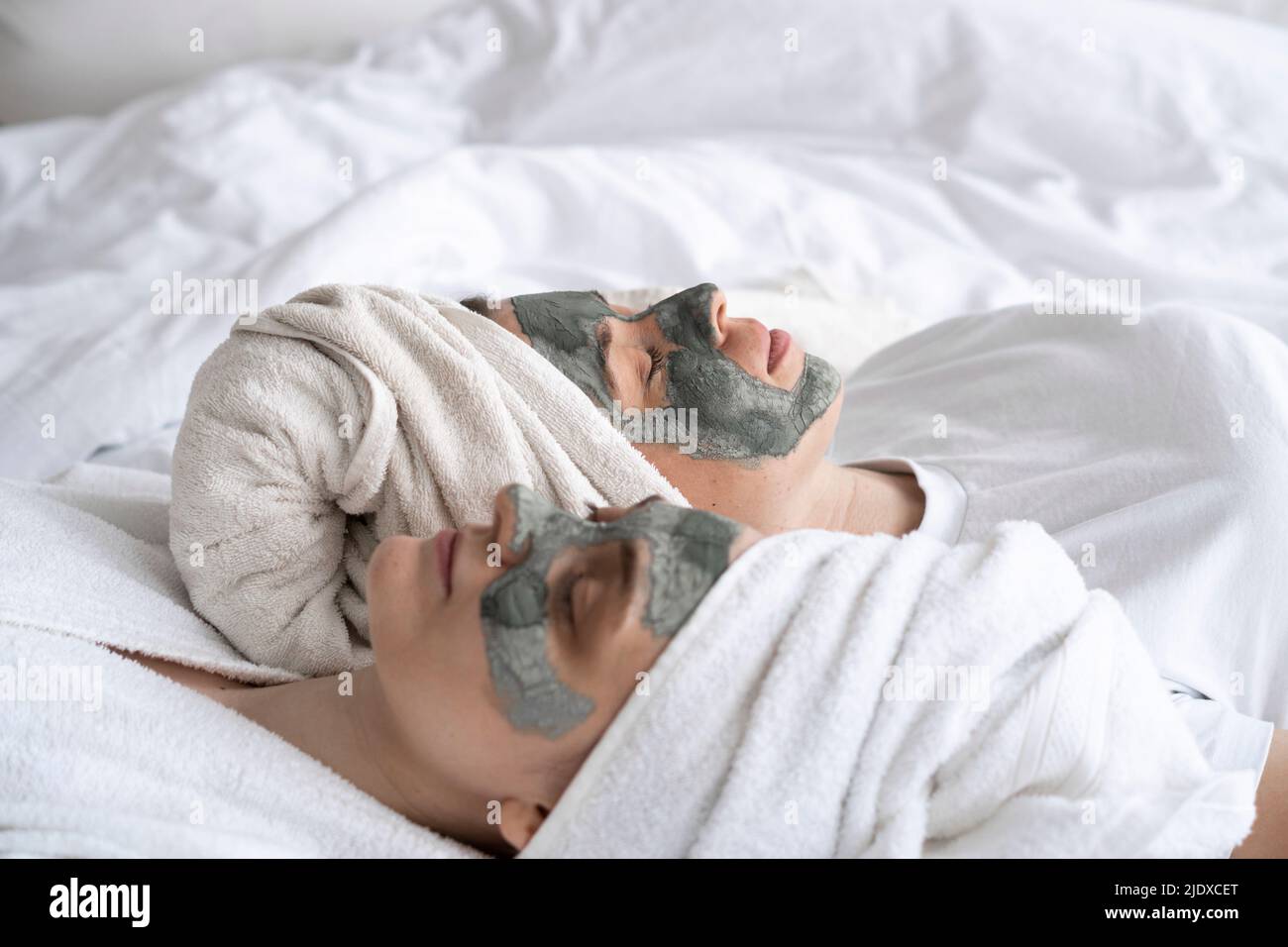 Amis portant un masque facial allongé sur le lit à la maison Banque D'Images