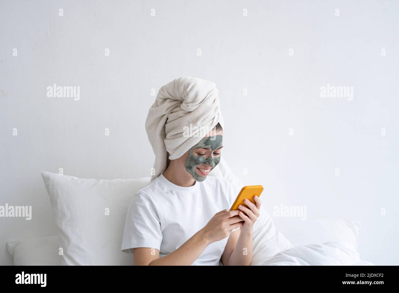 Femme heureuse portant un masque facial avec un smartphone dans la chambre Banque D'Images