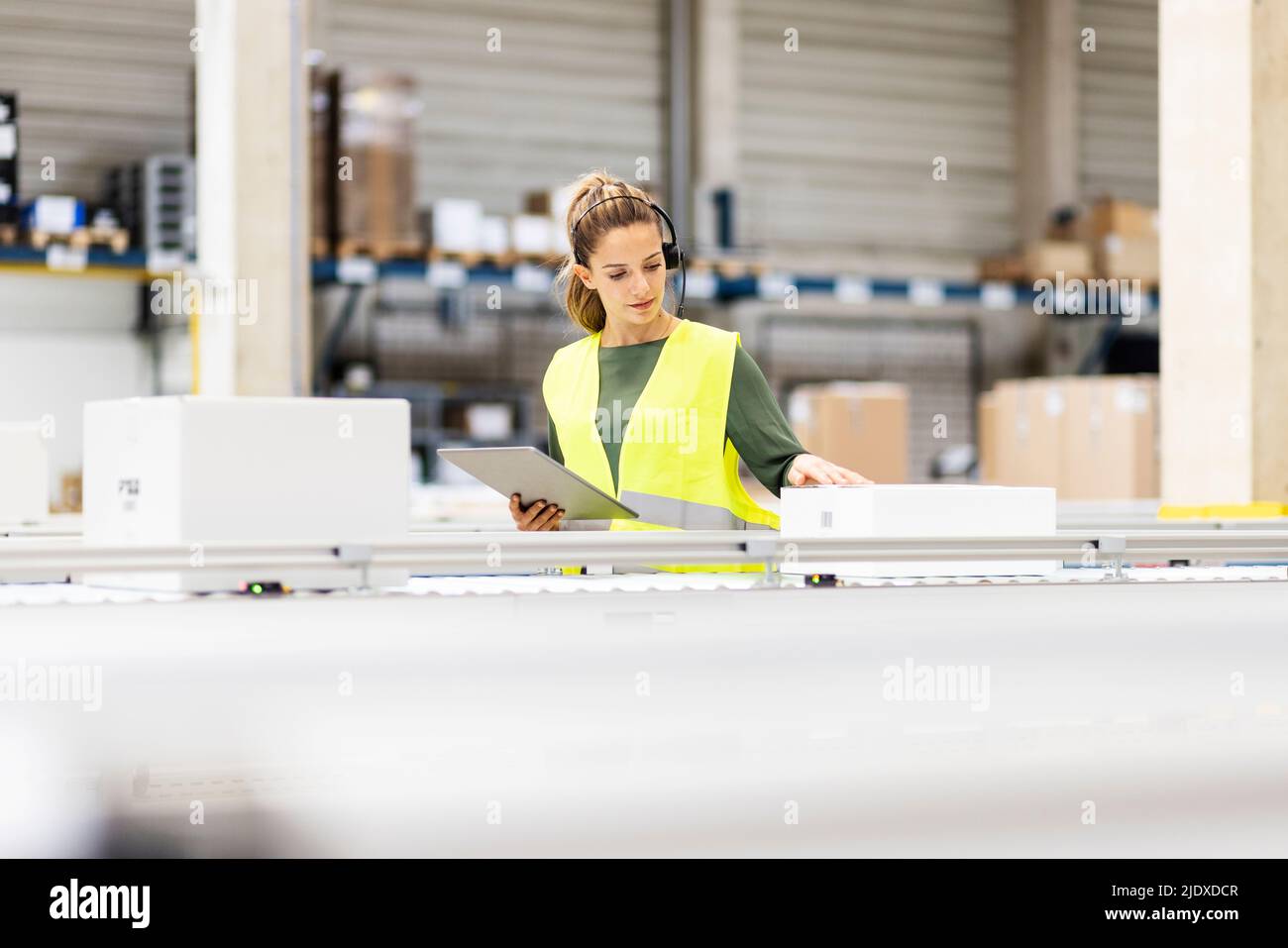 Jeune employé avec une tablette PC examinant la boîte sur le tapis transporteur dans l'entrepôt Banque D'Images