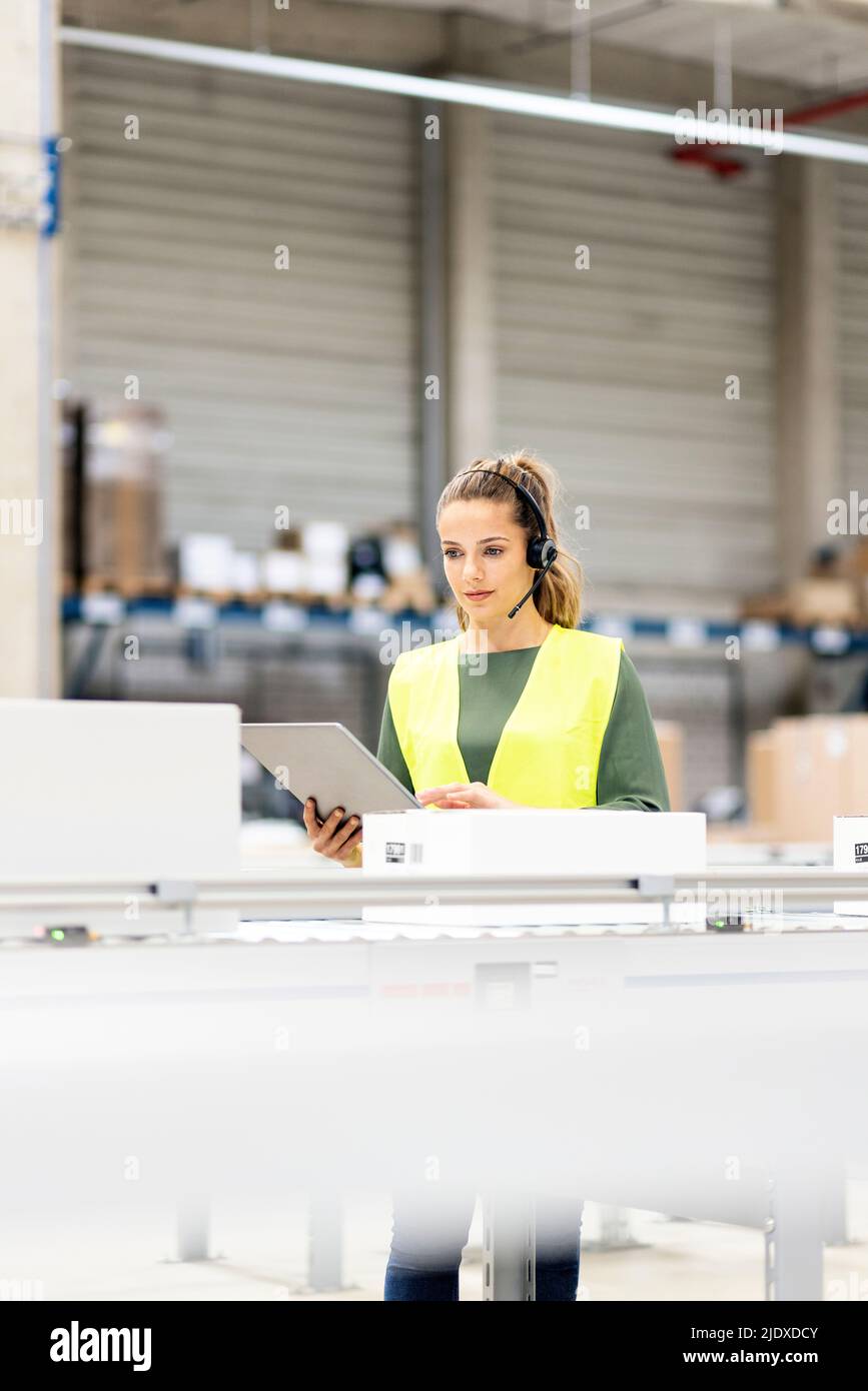 Employé portant un casque tenant une tablette PC sur le tapis transporteur de l'entrepôt Banque D'Images