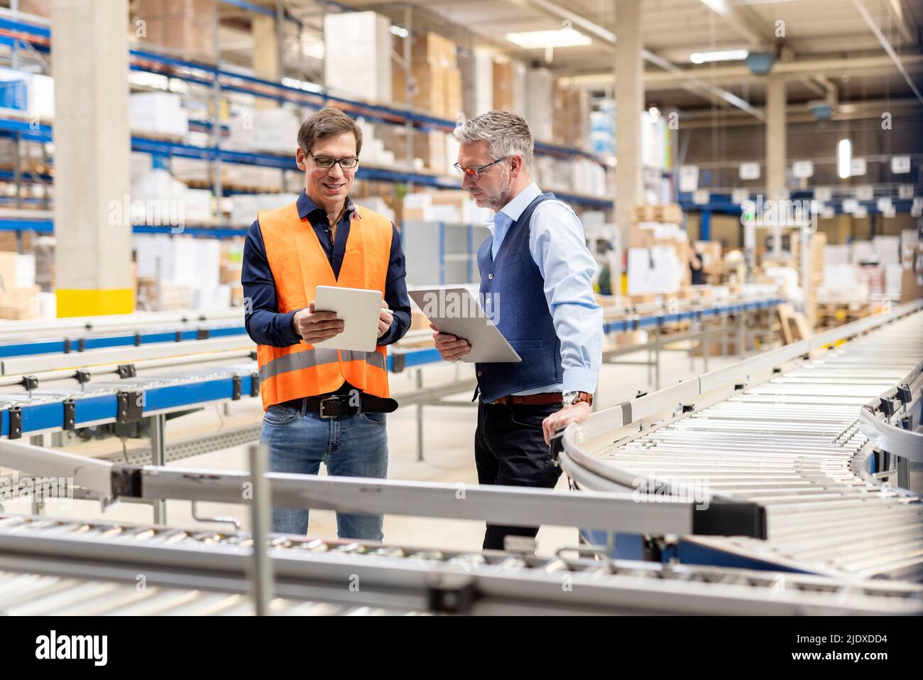 Un employé parle de tablette avec un responsable se tenant près du tapis transporteur dans l'entrepôt Banque D'Images