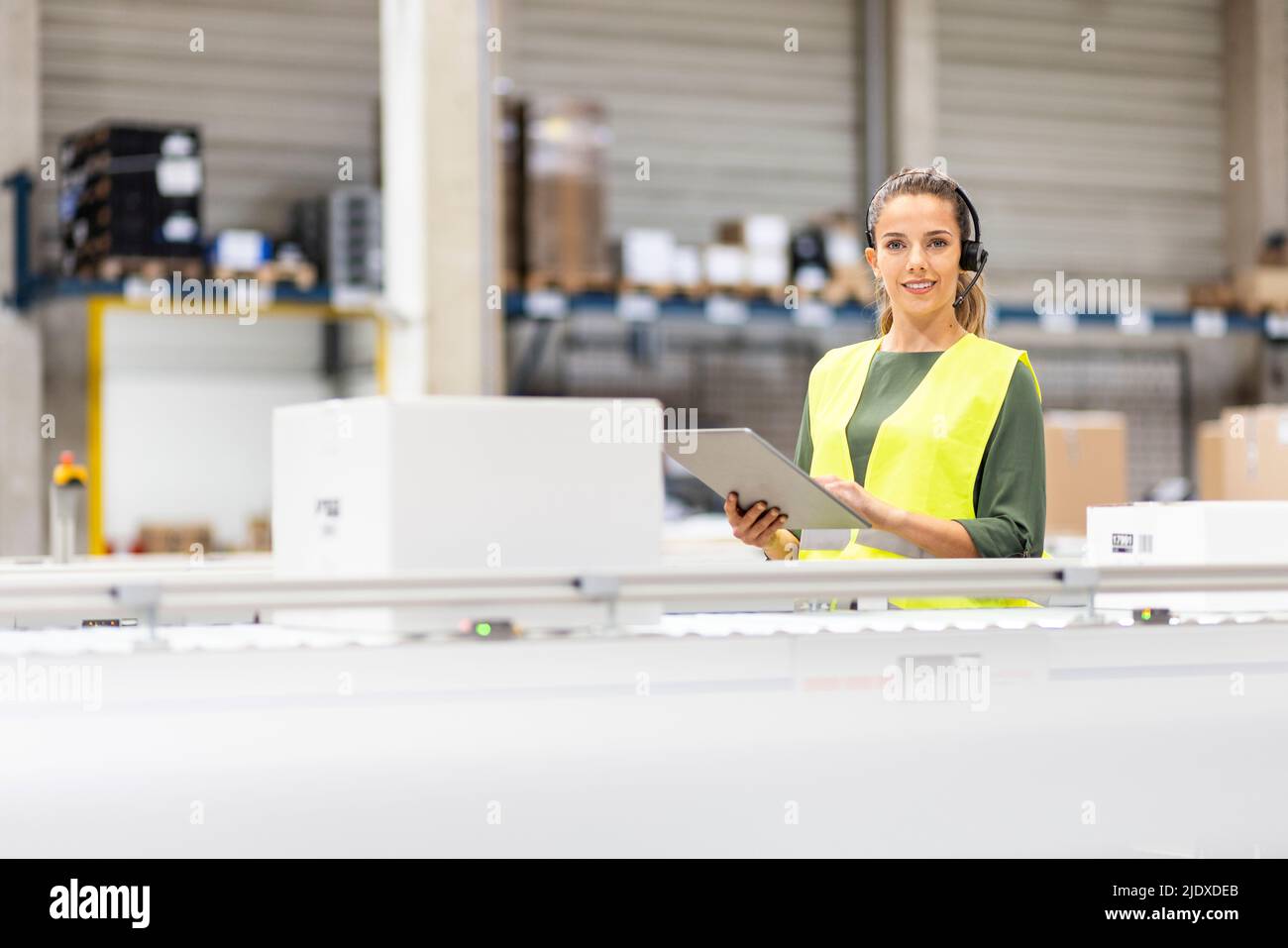 Jeune travailleur souriant avec un Tablet PC à côté du tapis roulant dans l'entrepôt Banque D'Images