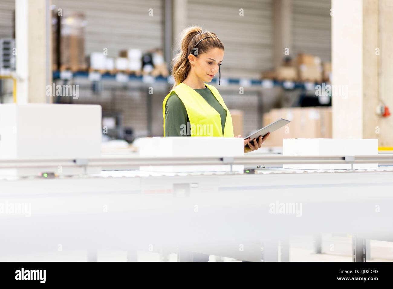 Jeune employé tenant une boîte d'analyse pour PC tablette sur le tapis transporteur dans un entrepôt Banque D'Images