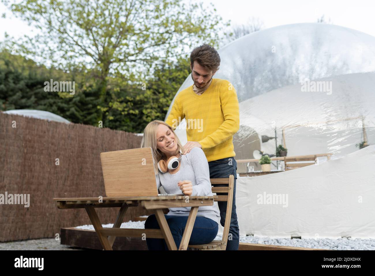 Homme donnant un massage des épaules à une petite amie assise avec un ordinateur portable Banque D'Images