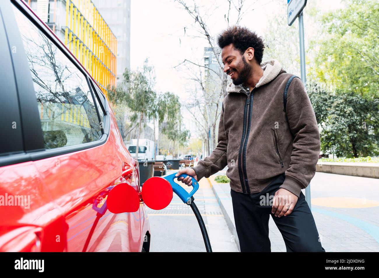Un homme heureux charge la voiture électrique à la gare Banque D'Images