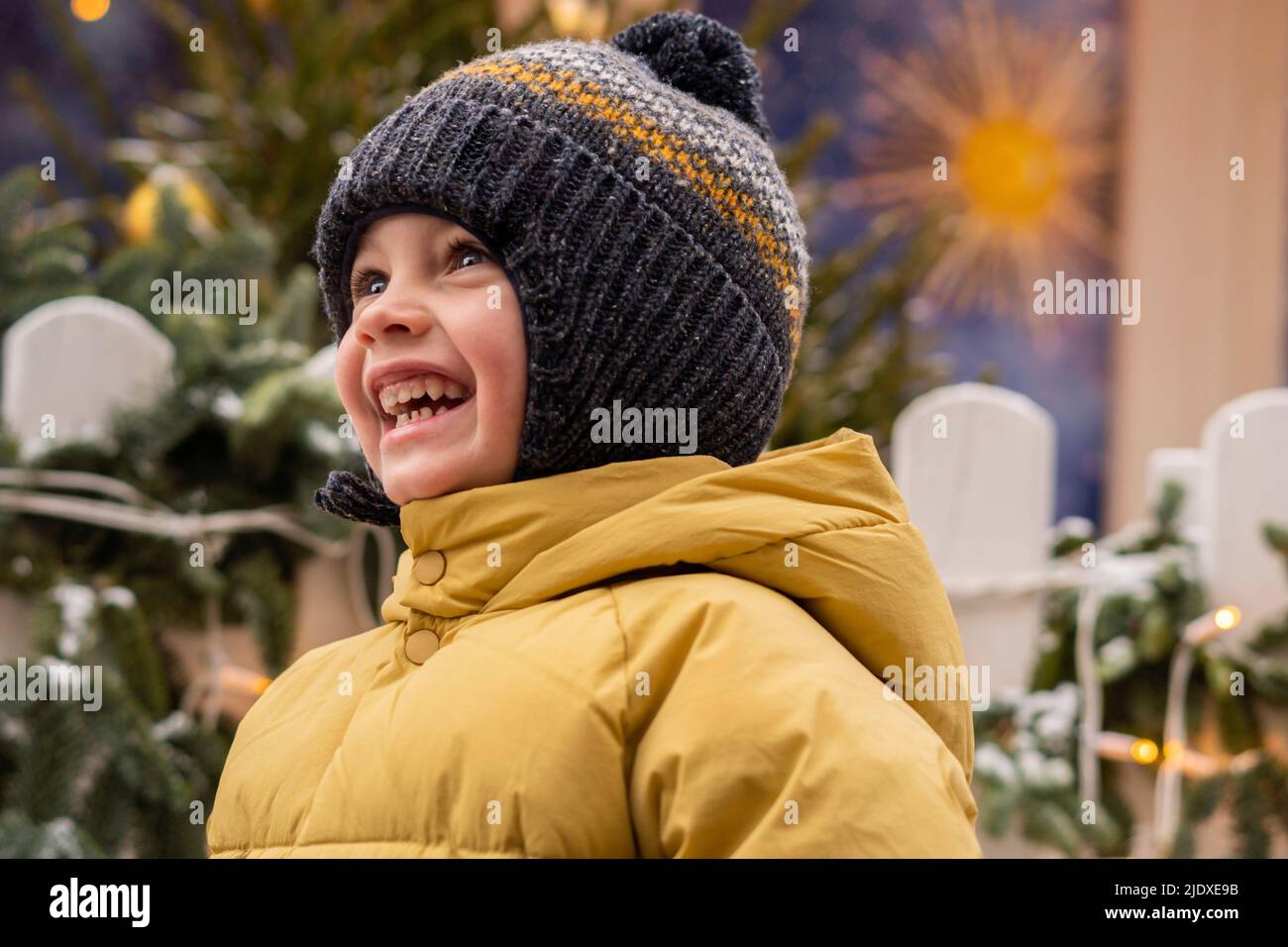 Joyeux garçon dans une veste matelassée jaune portant un chapeau en tricot Banque D'Images