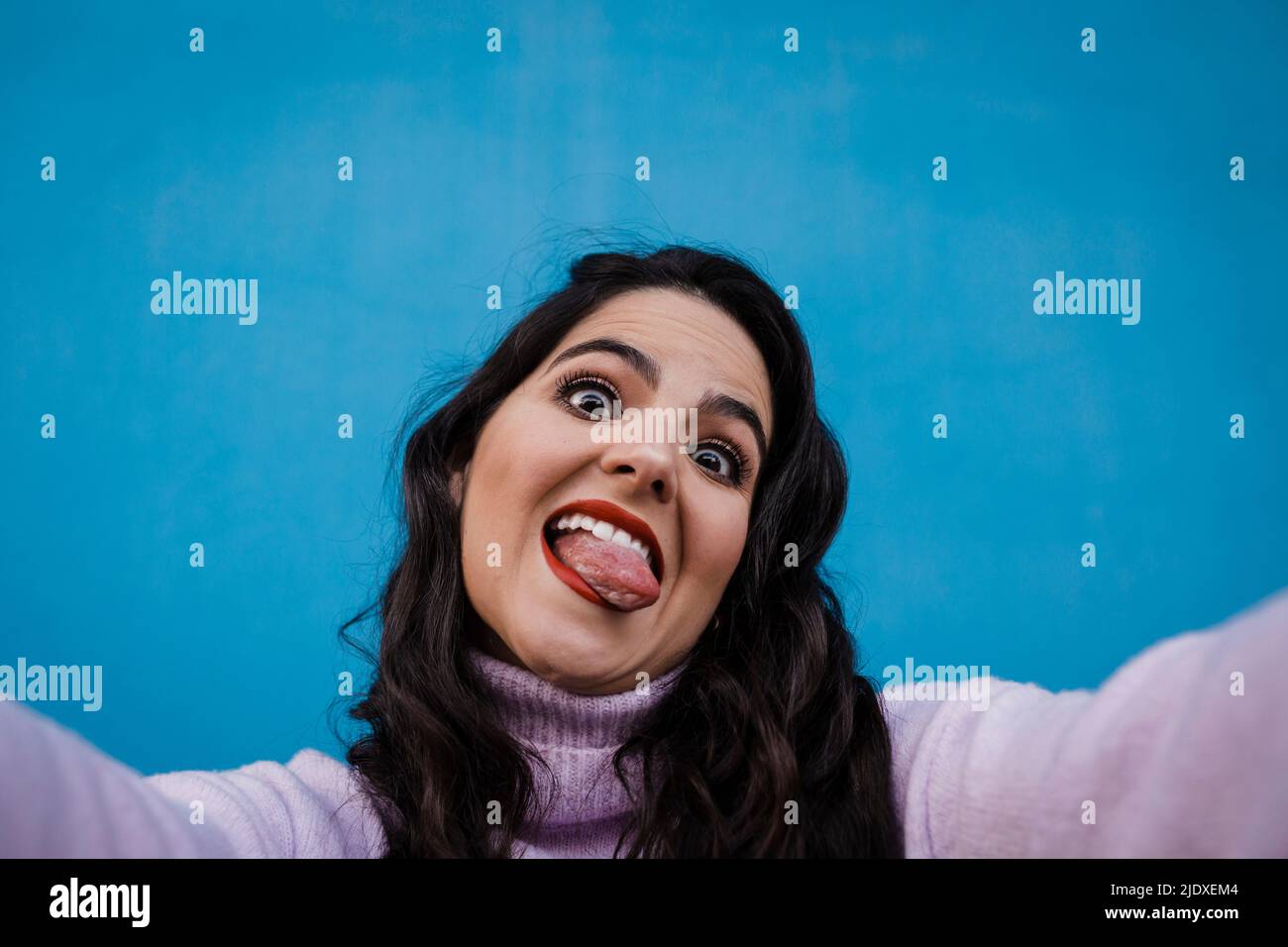 Joueur de la femme heureuse qui colle la langue en prenant le selfie devant le mur bleu Banque D'Images