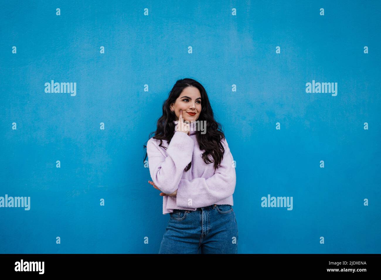 Jeune femme attentionnée debout devant le mur bleu Banque D'Images