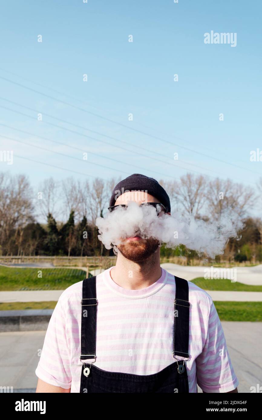 Homme exhalant de la fumée debout le jour ensoleillé Banque D'Images