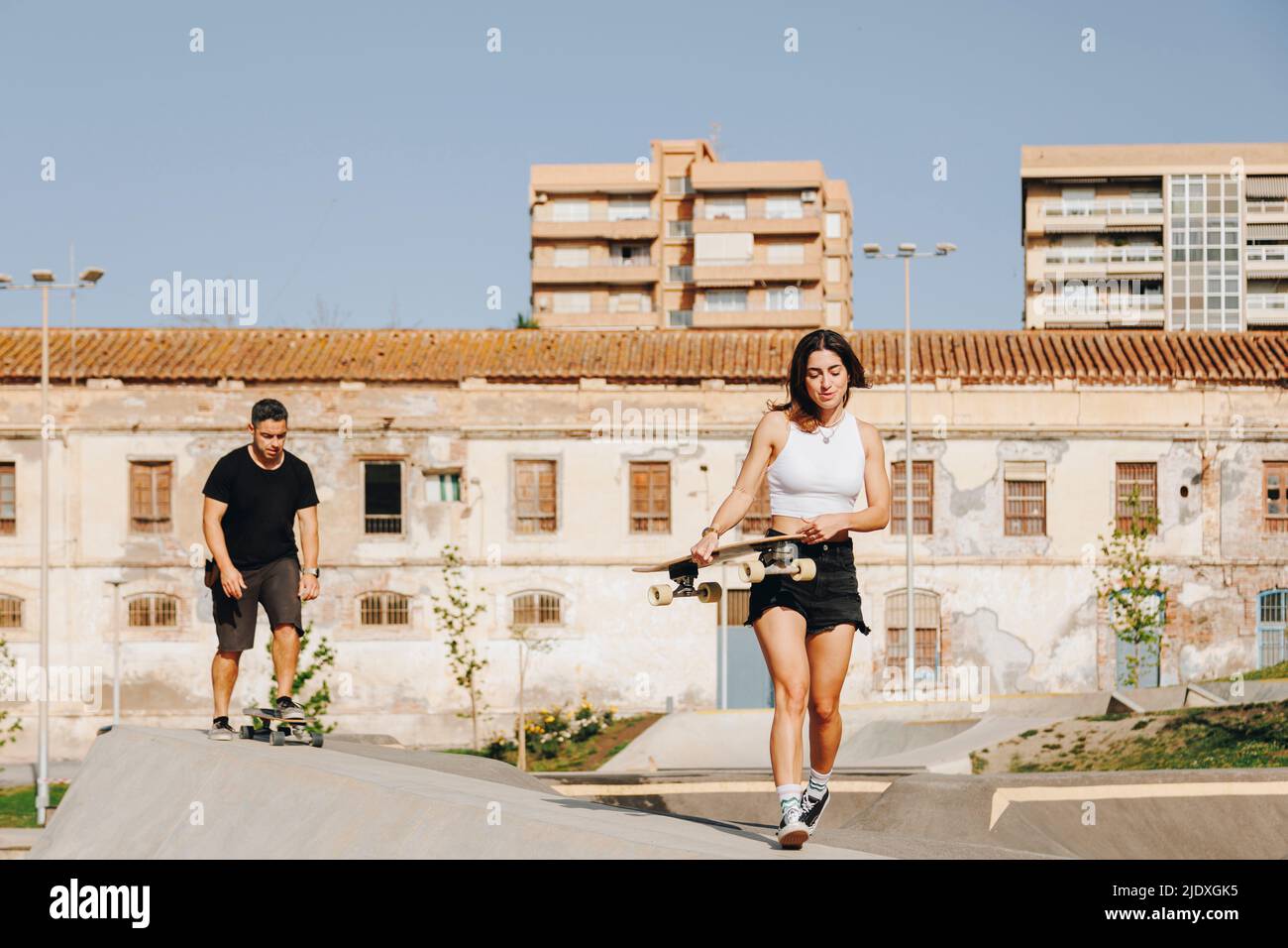 Jeune femme tenant une planche à roulettes marchant sur une rampe de sport devant l'homme Banque D'Images