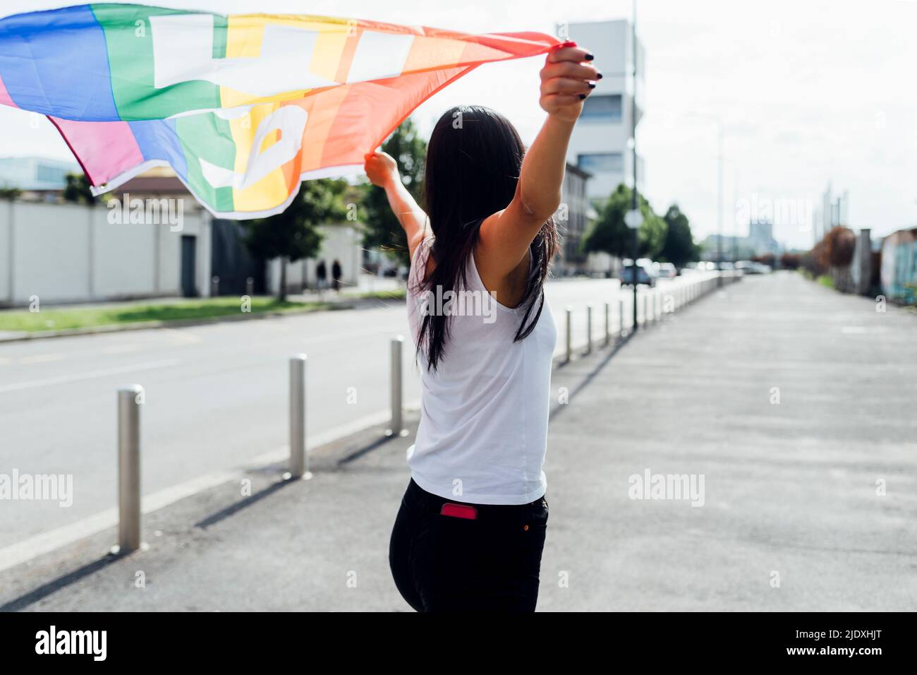 Jeune femme debout avec le drapeau arc-en-ciel le jour ensoleillé Banque D'Images