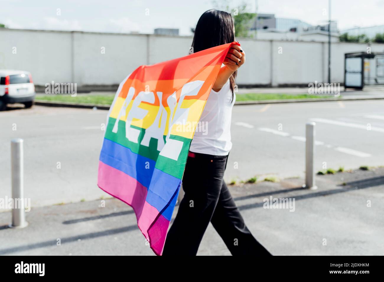 Femme avec drapeau arc-en-ciel marchant le jour ensoleillé Banque D'Images