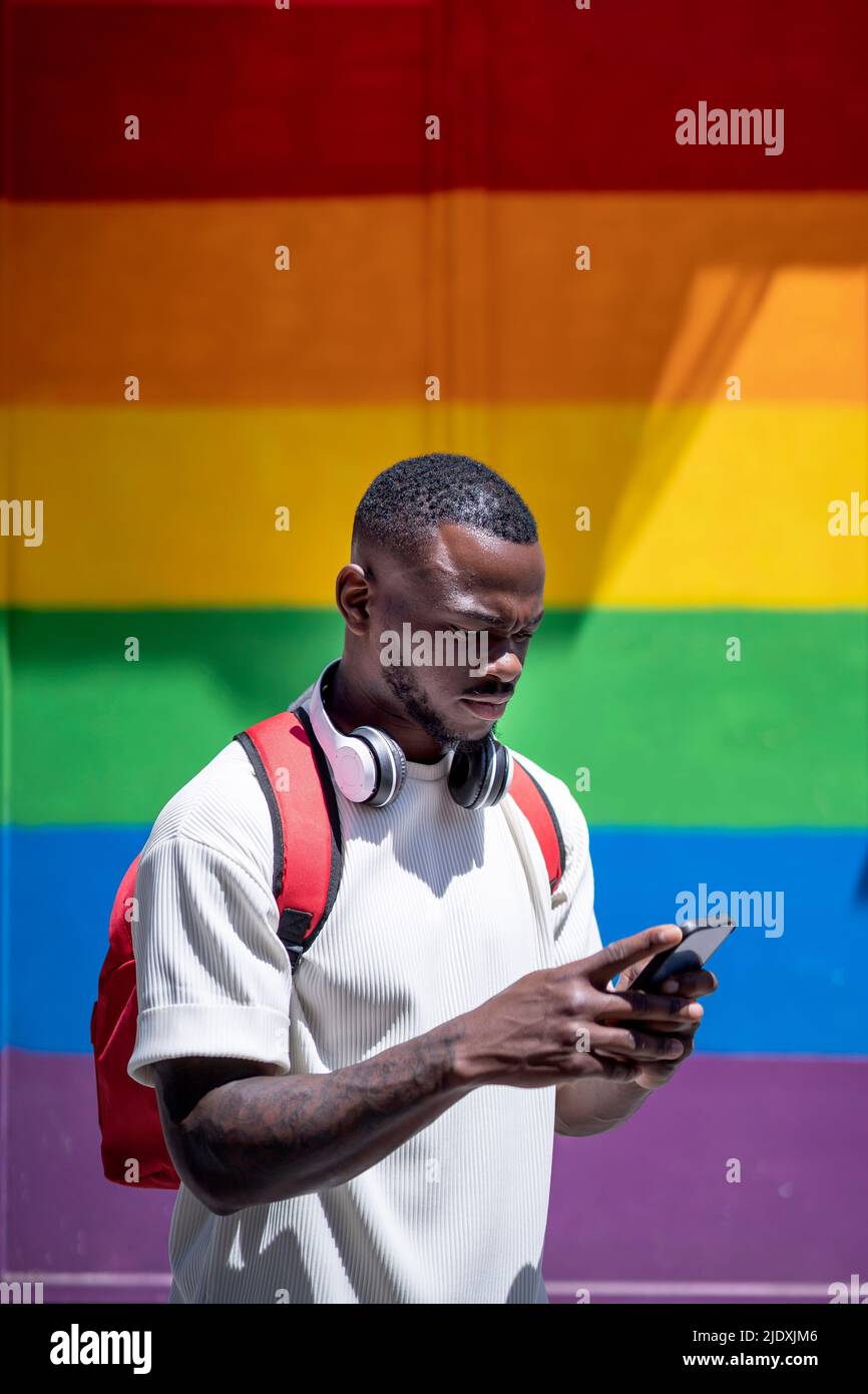 Jeune homme utilisant un smartphone devant un mur arc-en-ciel Banque D'Images