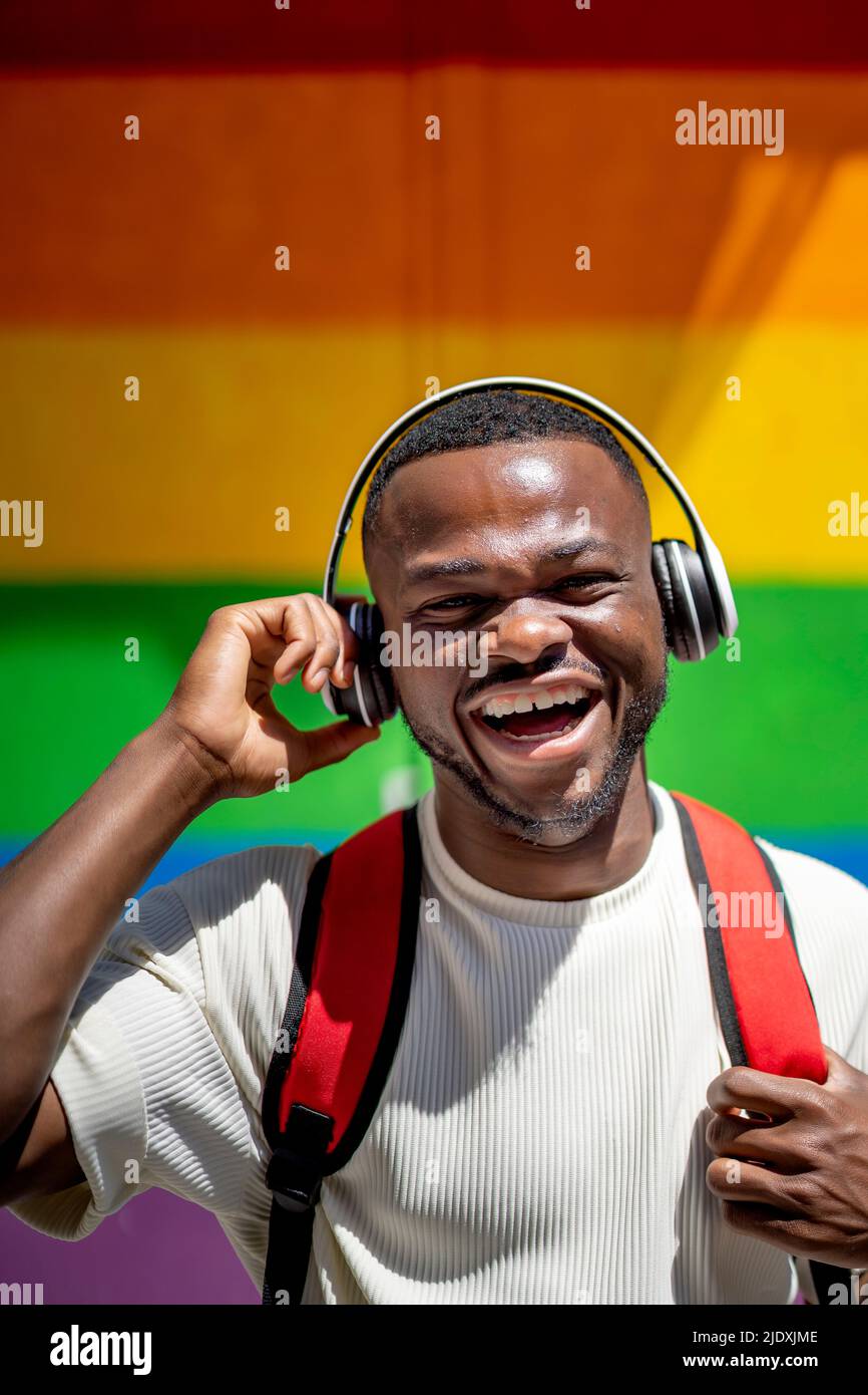 Un homme heureux avec un casque sans fil devant le mur arc-en-ciel Banque D'Images