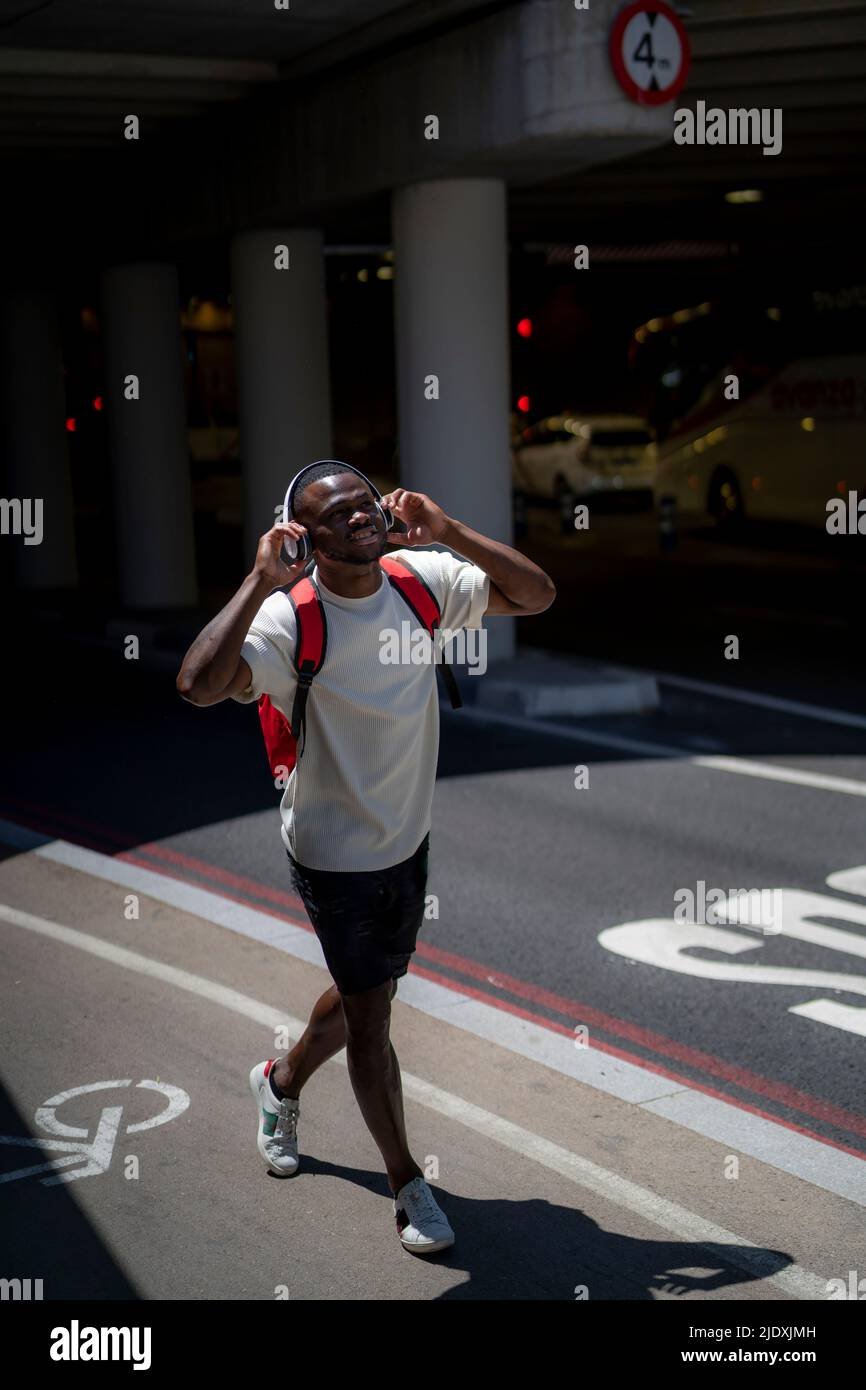 Un jeune homme écoute de la musique avec un casque sans fil qui marche sur la route Banque D'Images