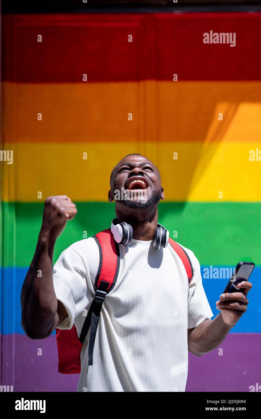 Un jeune homme heureux criant devant le mur de l'arc-en-ciel Banque D'Images