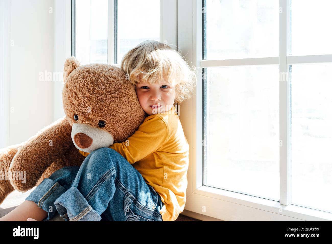 Garçon avec un jouet ours en peluche assis près de la fenêtre à la maison Banque D'Images