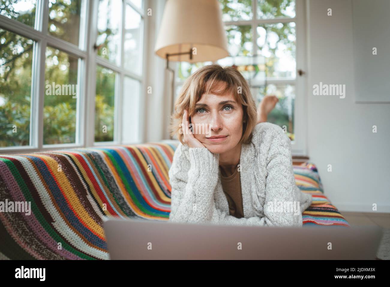 Femme mûre et attentionnés avec un ordinateur portable allongé sur un canapé à la maison Banque D'Images
