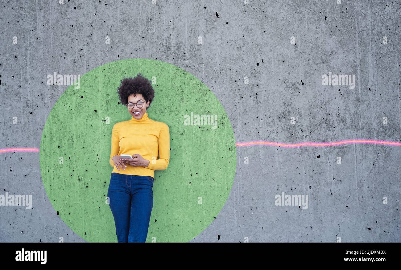 Femme qui utilise un smartphone penchée sur un mur avec un cercle vert Banque D'Images