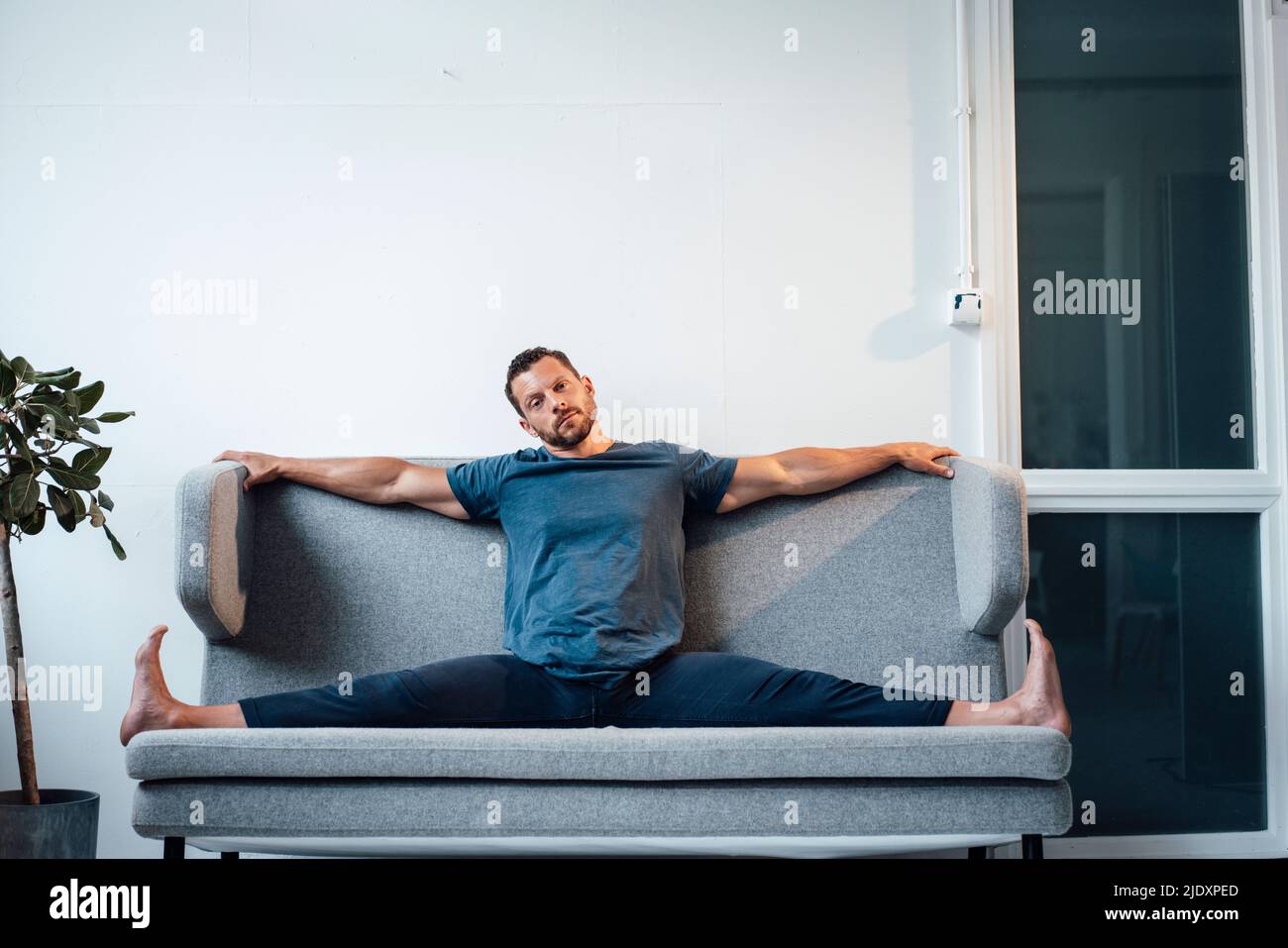 Homme avec les jambes séparées assis sur le canapé à la maison Banque D'Images