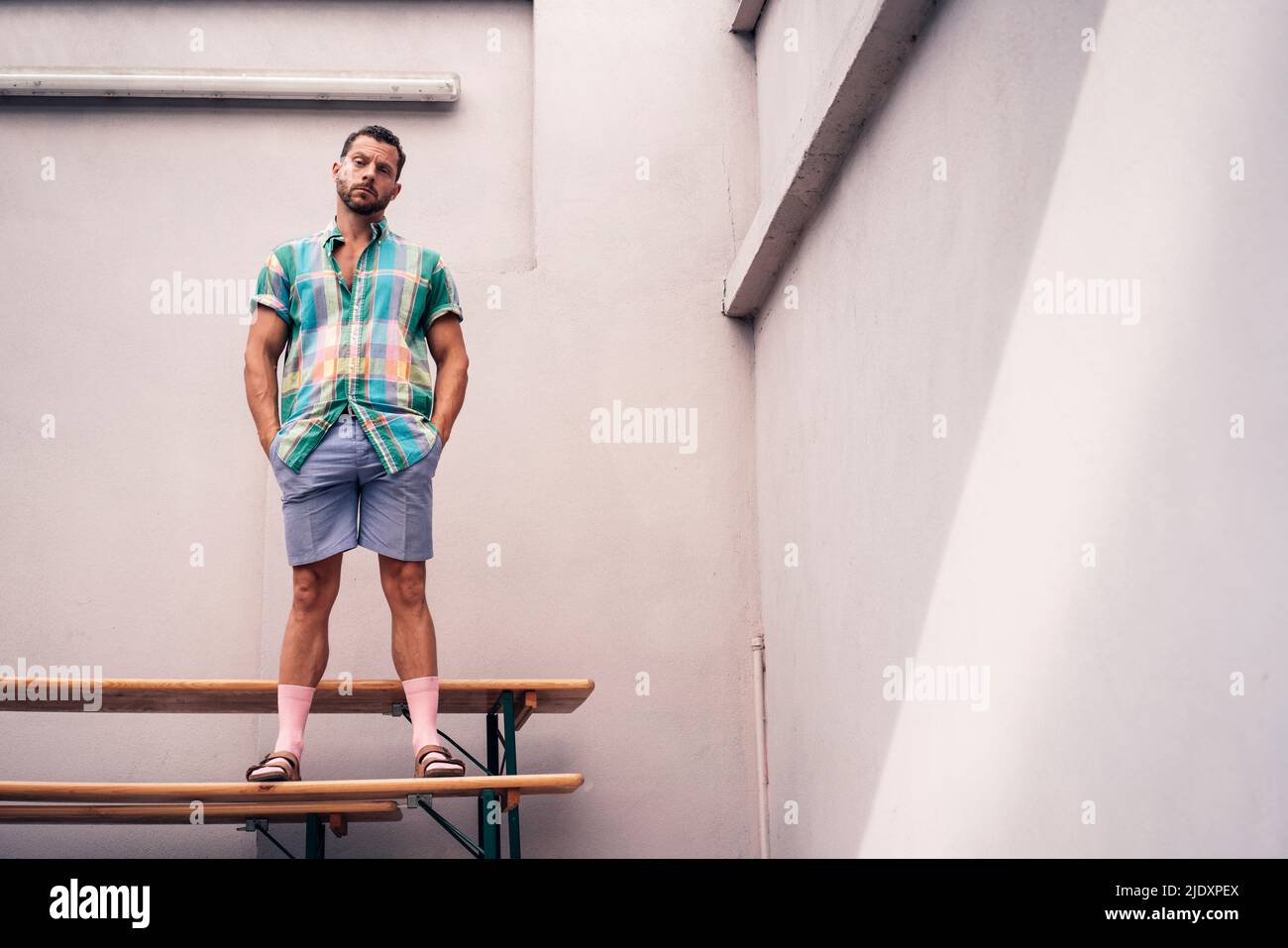 Homme mûr avec les mains dans les poches debout sur le banc devant le mur Banque D'Images