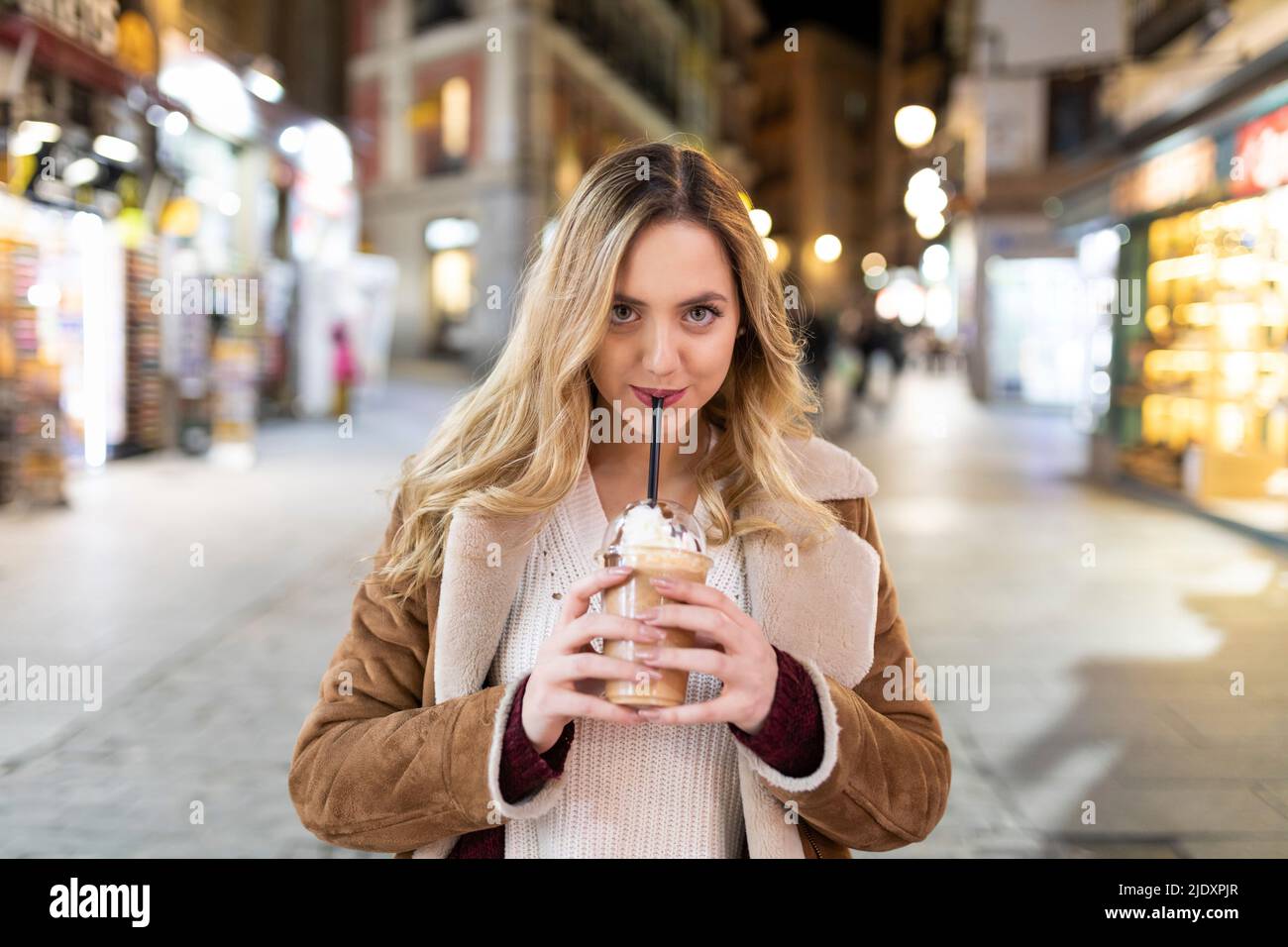 Une jeune femme boit dans une tasse jetable dans la rue en ville Banque D'Images