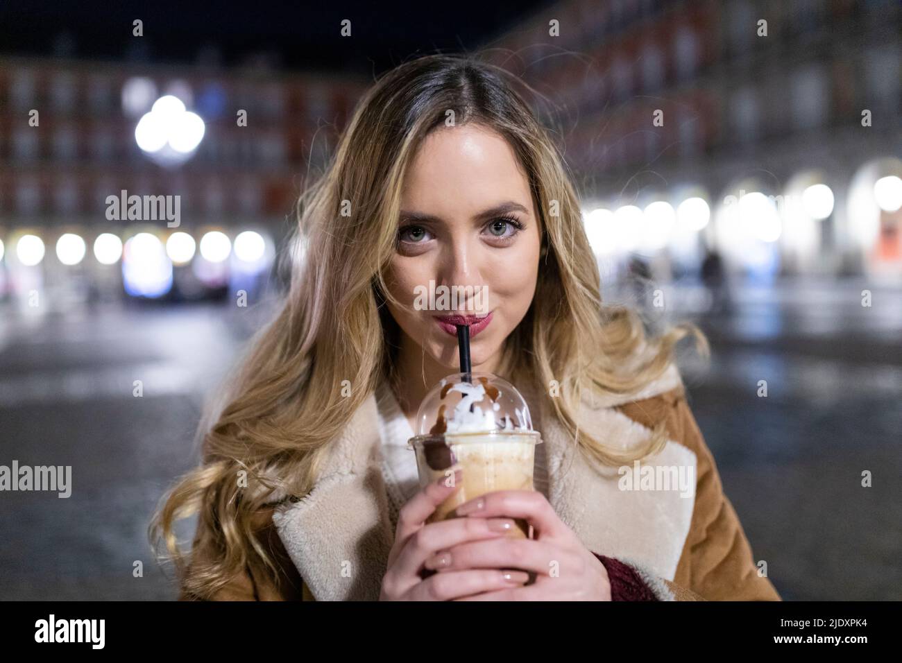 Une jeune femme boit dans une tasse jetable en ville la nuit Banque D'Images