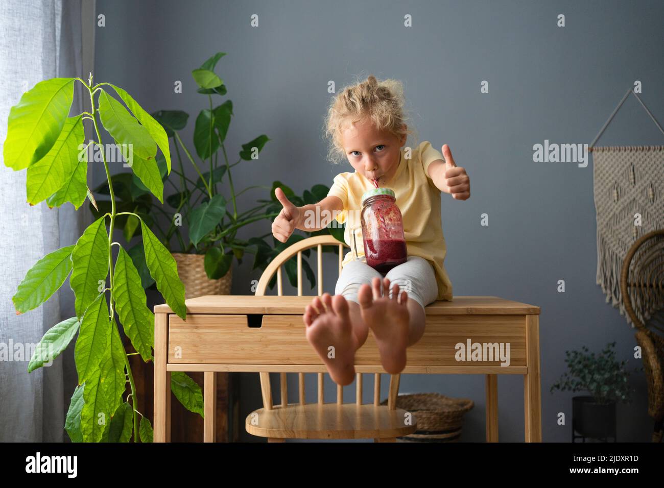 Une fille qui boit du smoothie montrant des pouces vers le haut geste assis sur une table Banque D'Images
