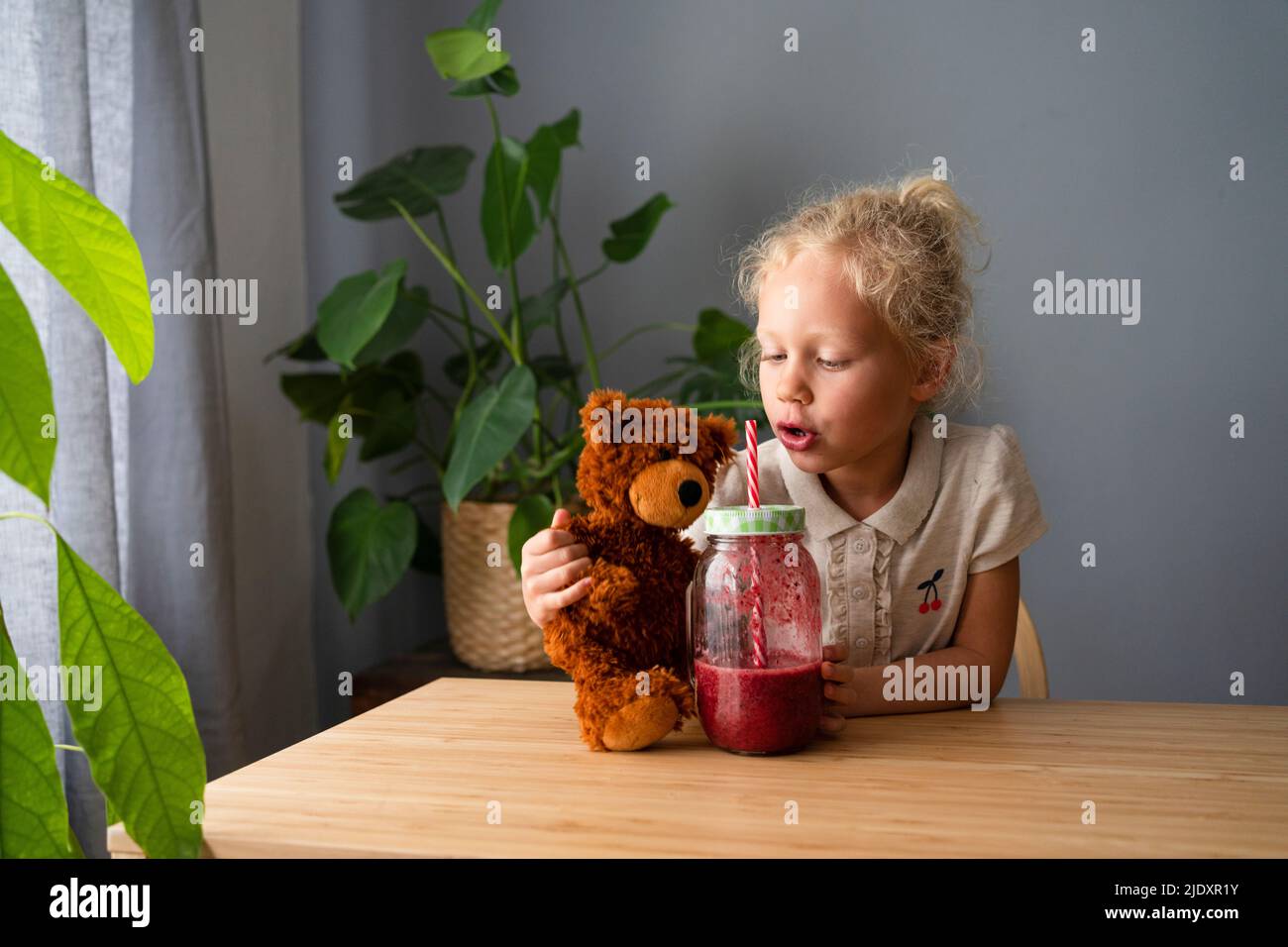 Fille avec un pot à smoothie et un ours en peluche sur la table à la maison Banque D'Images