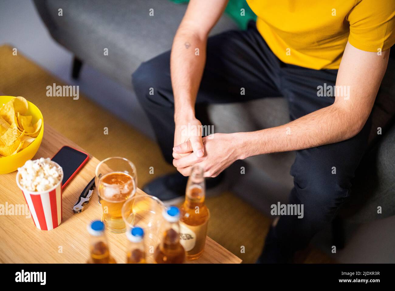 Un jeune homme assis sur un canapé près d'une table basse avec une bouteille de bière et du pop-corn à la maison Banque D'Images