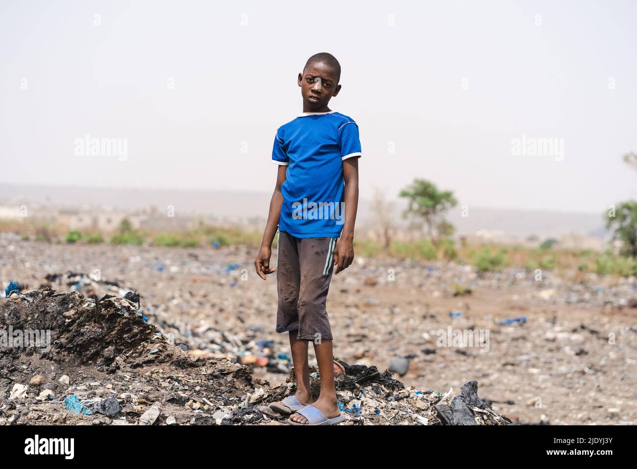 Un garçon africain désespéré avec des stands tristement au milieu d'un champ d'ordures, symbolisant les problèmes environnementaux causés par l'élimination incorrecte des ordures a Banque D'Images