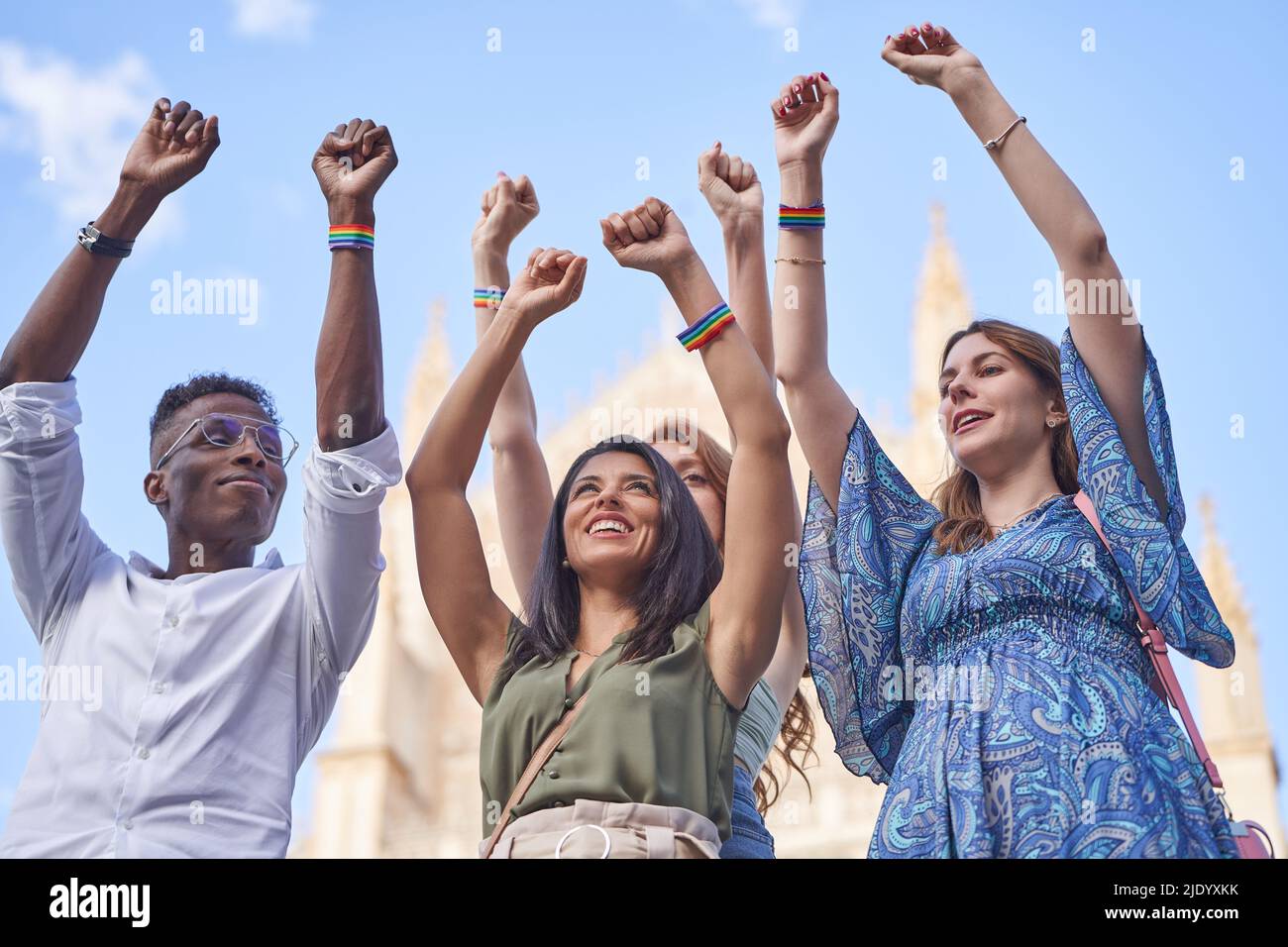 Groupe de personnes multiraciales debout ensemble à l'extérieur tout en levant les mains avec les bracelets de drapeau arc-en-ciel LGBT. Concept de diversité, d'égalité et d'unité. Banque D'Images