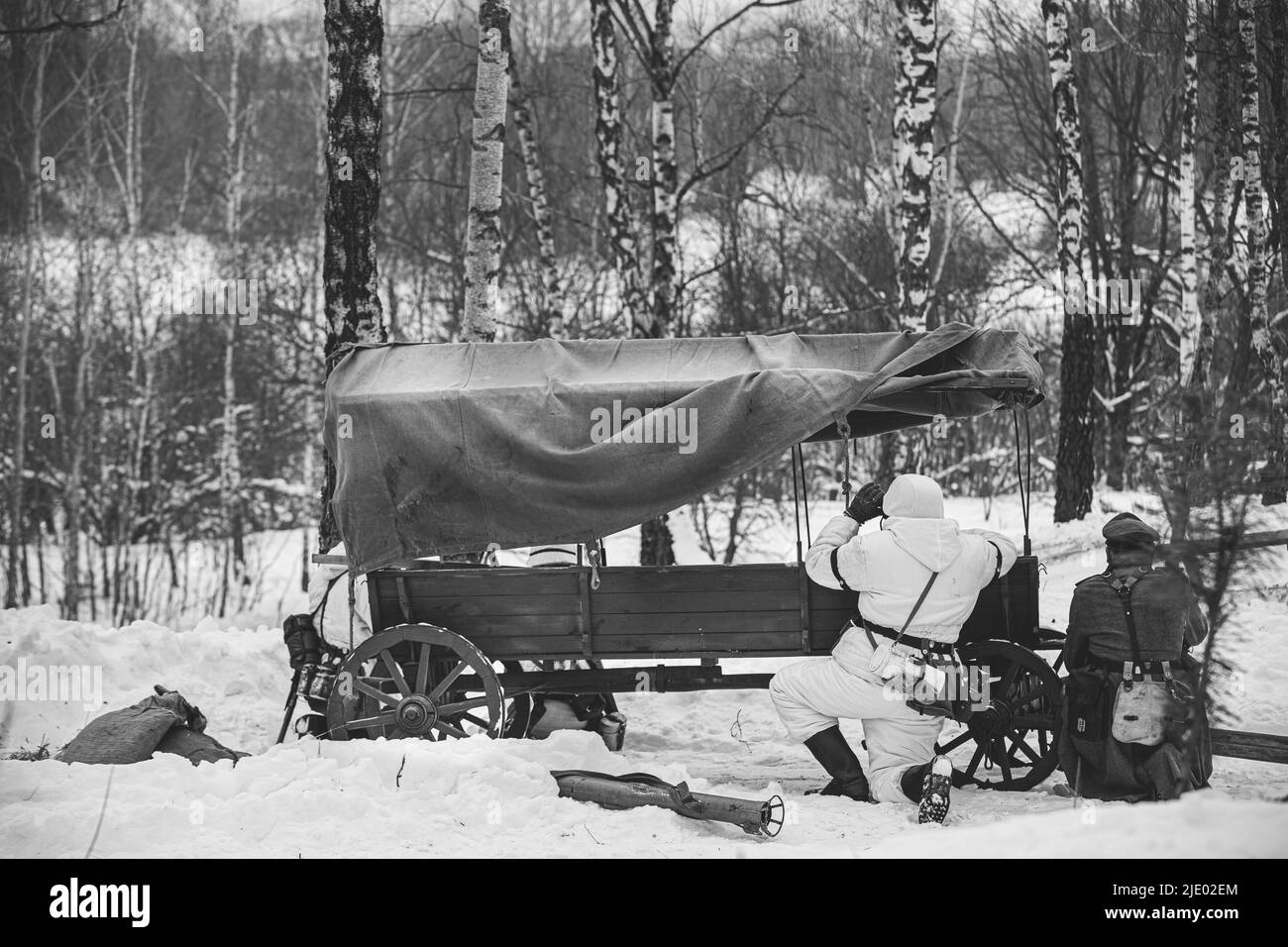 Soldat d'infanterie de Wehrmacht allemand dans les soldats de la Seconde Guerre mondiale assis à Ambush près de la charrette paysanne dans la forêt d'hiver et regardant les jumelles de l'ancienne armée Banque D'Images