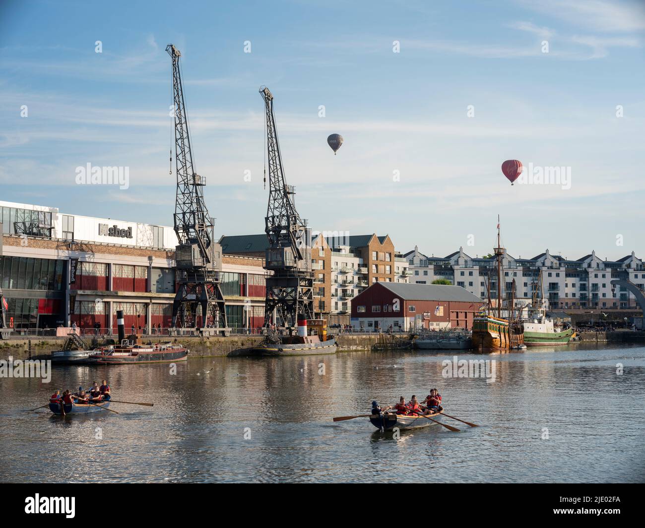 Des ballons à air chaud flottent au-dessus des grues, des bateaux à rames et du mShed dans la zone portuaire flottante de Bristol lors d'une soirée d'été ensoleillée. Banque D'Images