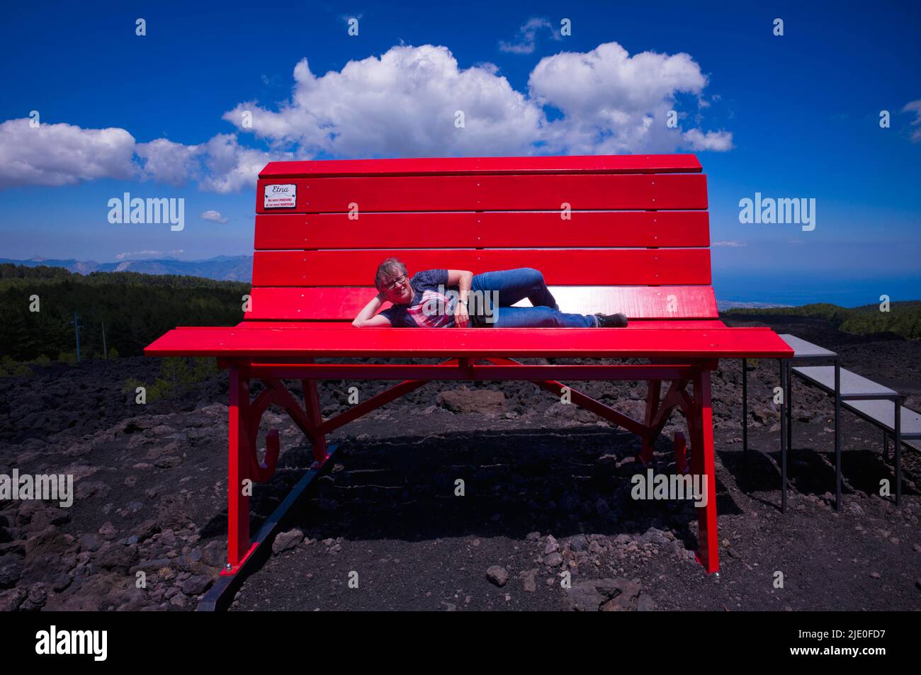 Femme âgée couchée sur un immense banc rouge, projet communautaire du grand banc, grand banc numéro 200, Etna, Grande Panchina, Linguaglossa, Sicile, Italie Banque D'Images