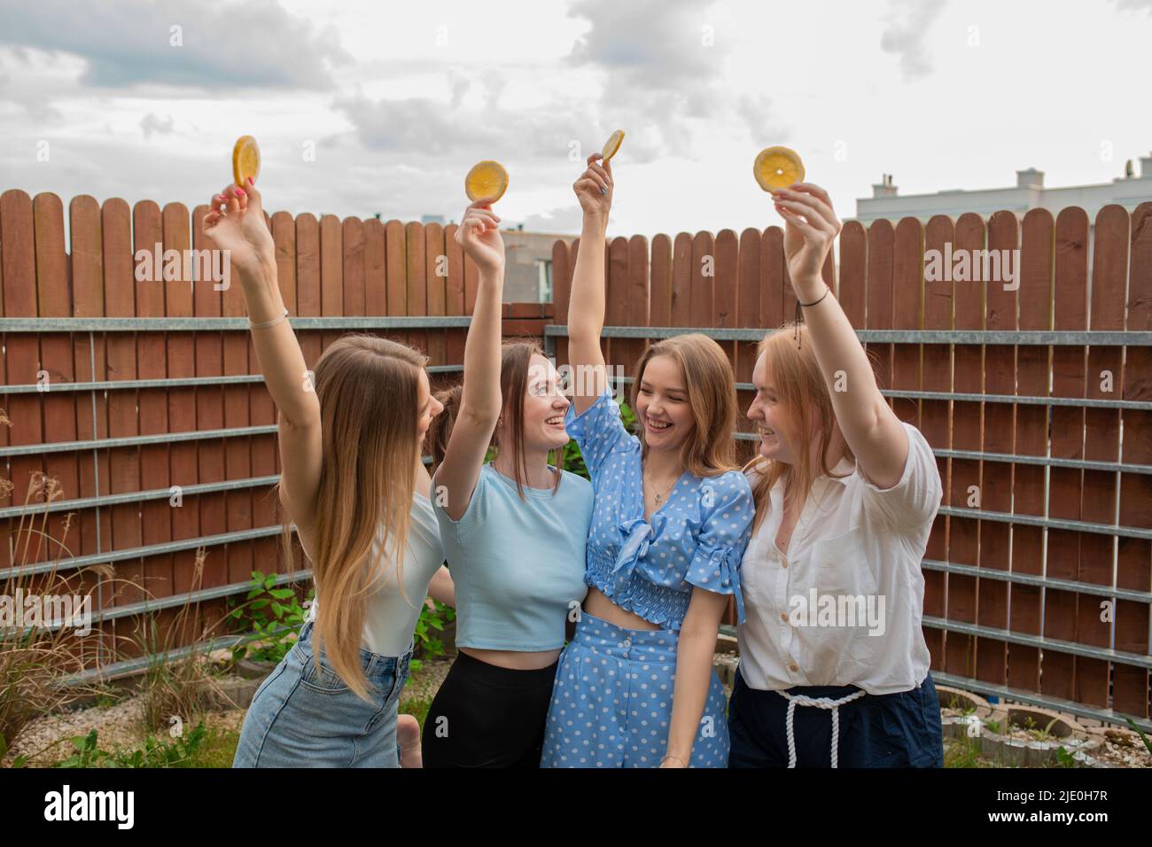 Riant les jeunes filles debout ensemble, levant les mains avec des oranges et regardant les uns les autres, ciel arrière-plan. S'amuser et profiter de l'extérieur Banque D'Images