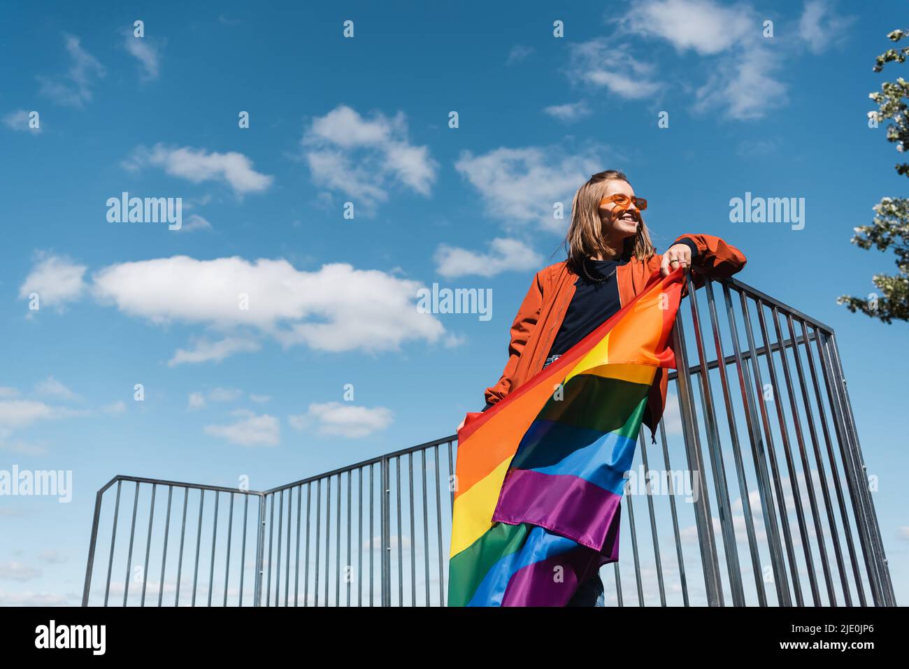 vue en contre-angle d'une femme souriante avec drapeau lgbt contre ciel bleu nuageux Banque D'Images